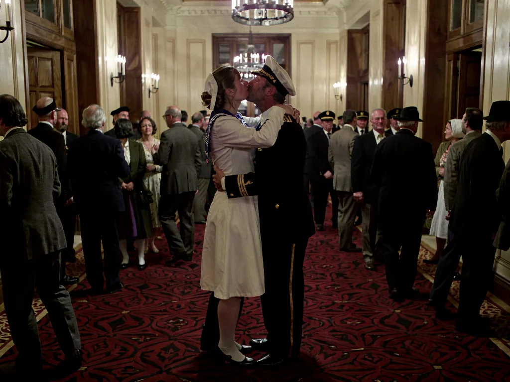 Klein LoRA image-to-image output named Overlook Waltz, a sailor and nurse kissing in a grand warm hotel hallway with patterned carpet and wood-paneled shadows.